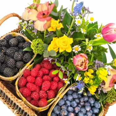 Plano cenital de cesta artesanal Naranjas de la China mostrando compartimentos de moras, frambuesas y arándanos y flores variadas.